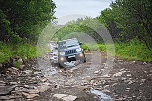 Suv car driving on a dirt off road with puddles and stones in the forest