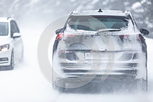 SUV car driving on snowy slippery road inside the forest, having registration number insivisible due to snow