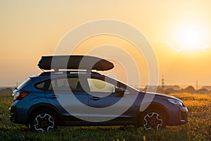 SUV car with roof rack luggage container for off road travelling parked at roadside at sunset. Road trip and getaway concept