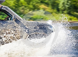 SUV is driving along a shallow river and strong splashes