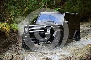 SUV or offroad car in black color crossing water stream Car racing with creek on way. Offroad race in forest Extreme