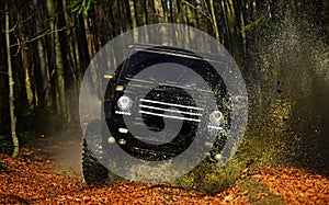 SUV or offroad car on path covered with leaves crossing puddle with dirty water splash. Offroad race on fall nature