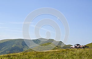 SUV and two motorcycles stands at peak of the hill with beautiful mountains at background