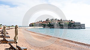 Sveti Stefan island in Budva in a beautiful summer day, Montenegro. Luxury sand beach with wooden chaise-longue chairs and