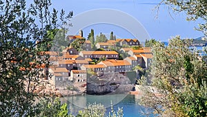 Sveti Stefan - Panoramic view framed by tree branches of idyllic island Sveti Stefan, Budva Riviera, Montenegro