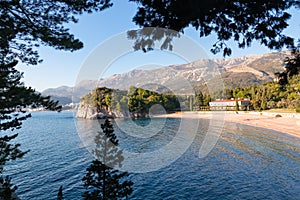 Sveti Stefan - Scenic view on turquoise water of idyllic Queens beach framed by tree branches near Sveti Stefan, Budva Riviera