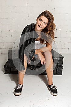 Swag woman with a black jacket over her shoulder sits on pallets. White brick wall, not isolated