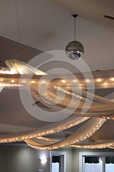 Swags of lights in tulle with silver disco ball hanging from white ceiling