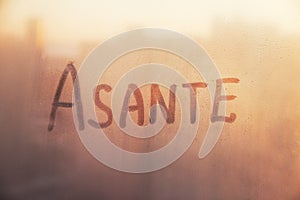 Swahili word Asante thanks in english are painted on wet orange sunrise glass of window