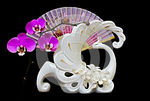 Decorative swan shape flower vase with pink orchids and oriental folding fan  on dark background