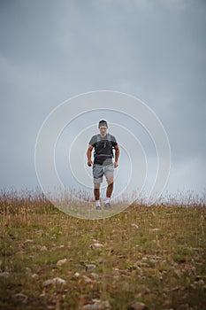 Swarthier type of man is running down a gravel hill, checking his every step to avoid injury. Active athlete runs over challenging