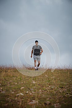 Swarthier type of man is running down a gravel hill, checking his every step to avoid injury. Active athlete runs over challenging