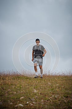 Swarthier type of man is running down a gravel hill, checking his every step to avoid injury. Active athlete runs over challenging