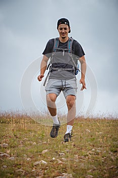 Swarthier type of man is running down a gravel hill, checking his every step to avoid injury. Active athlete runs over challenging