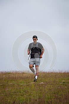 Swarthier type of man is running down a gravel hill, checking his every step to avoid injury. Active athlete runs over challenging