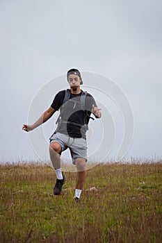 Swarthier type of man is running down a gravel hill, checking his every step to avoid injury. Active athlete runs over challenging