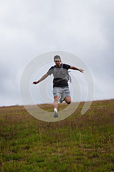 Swarthier type of man is running down a gravel hill, checking his every step to avoid injury. Active athlete runs over challenging