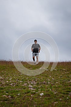 Swarthier type of man is running down a gravel hill, checking his every step to avoid injury. Active athlete runs over challenging