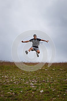 Swarthier type of man is running down a gravel hill, checking his every step to avoid injury. Active athlete runs over challenging