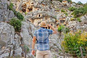 Swarthy caucasian european guy in plaid shirt and a hat stands back and looks in surprise at the ancient unique famous places