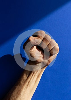 Swarthy rough mans hand with clenched fist on blue background. Cesar Chavez Day concept photo