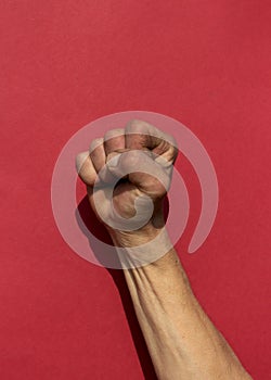 Swarthy rough mans hand with clenched fist on red background. Cesar Chavez Day concept