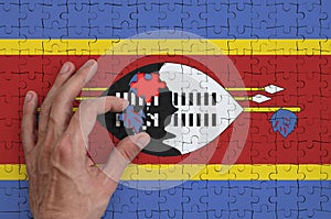 Swaziland flag is depicted on a puzzle, which the man`s hand completes to fold