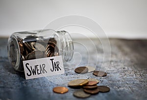 Swear Jar challenge concept with glass jar filled with coins, simple background