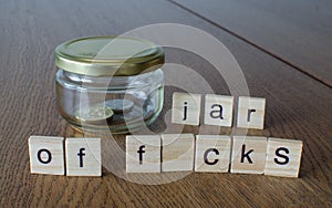 Swear jar `Jar of f*cks`on the wooden table background.