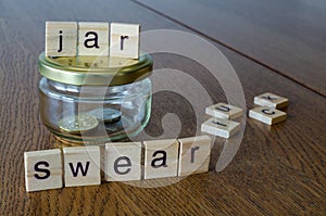 Swear jar on the wooden table background. Letters on wooden blocks