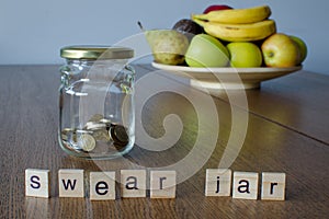 Swear jar on the wooden table with fruits background. Letters on wooden blocks