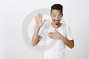 Swear to say truth. Studio shot of sincere happy african-american male with afro haircut, raising palm and holding hand