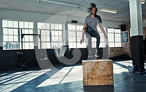 Sweat, smile and repeat. a young man doing jumping exercises on a wooden block in a gym.