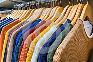 Sweaters of different colours on wooden hangers at clothing retail store or trift store. Clothing rental or donations