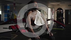 Sweating African American muscular sportsman wiping perspiration off forehead with towel exhaling and inhaling sitting