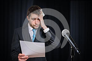 Sweating nervous speaker is afraid of public speech. Microphone in front.