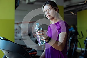 Sweating overweight girl run on treadmill at fitness gym and take bottle of water. Plus size woman do cardio workout on