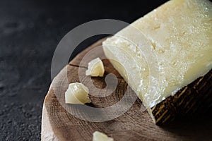 Sweating Spanish hard cheese manchego on wooden cut on dark rustic background