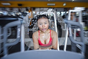 and sweaty Asian woman training hard at gym using elliptical pedaling machine gear in intense workout