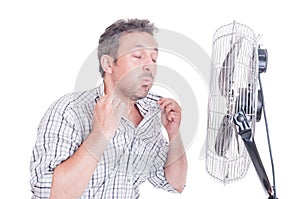 Sweaty man opening shirt in front of cooling fan