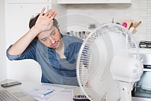 Sweaty man trying to refresh from heat with a fan