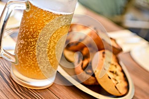 Sweaty mug of cold beer on a hot summer day, with bubbles visible, on a restaurant table with oiled bread in the background