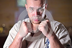 Sweaty and tired sportsman karate fighter stands in a fighting stance and looks at the camera