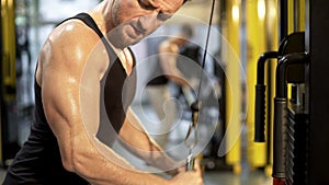 Sweaty upper body of guy doing pull-downs in gym, looking at his biceps, sport