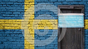 Sweden flag painted on brick wall and closed door with medical mask protected