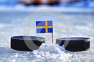 Švédska vlajka na špáradlo medzi dvoma hokejovými pukmi. Švédsko bude hrať na Svetovom pohári v skupine B. Majstrovstvá sveta 2019 IIHF