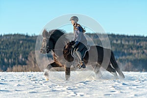 Swedish girl riding her Icelandic horse in deep snow and sunlight