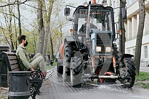 The sweeper disinfects the street. The man on the bench tucks his legs