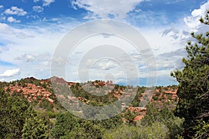 Sweeping landscape of Red Rock mountains and rock formations dotted with evergreen trees at Garden of the Gods in Colorado