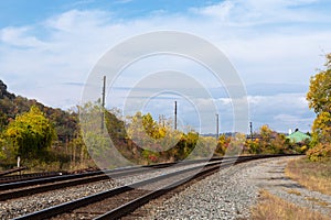 Sweeping view of railroad tracks running into the distance with seasonal fall colors, blue sky and clouds